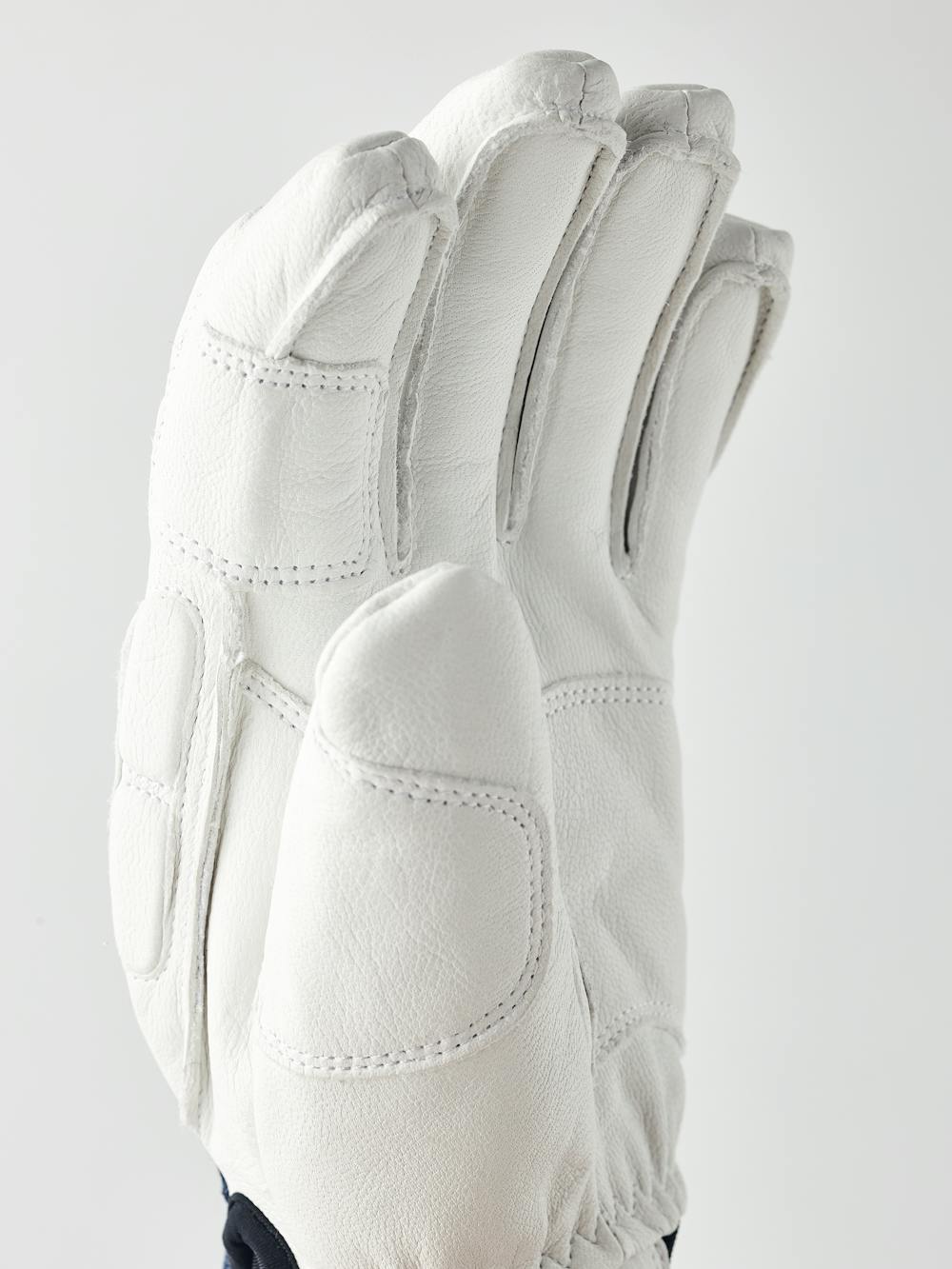 Vit skidhandske i getskinn och mörkblå tyg på bakhanden med stötdämpande paneler
 (2 av 6)