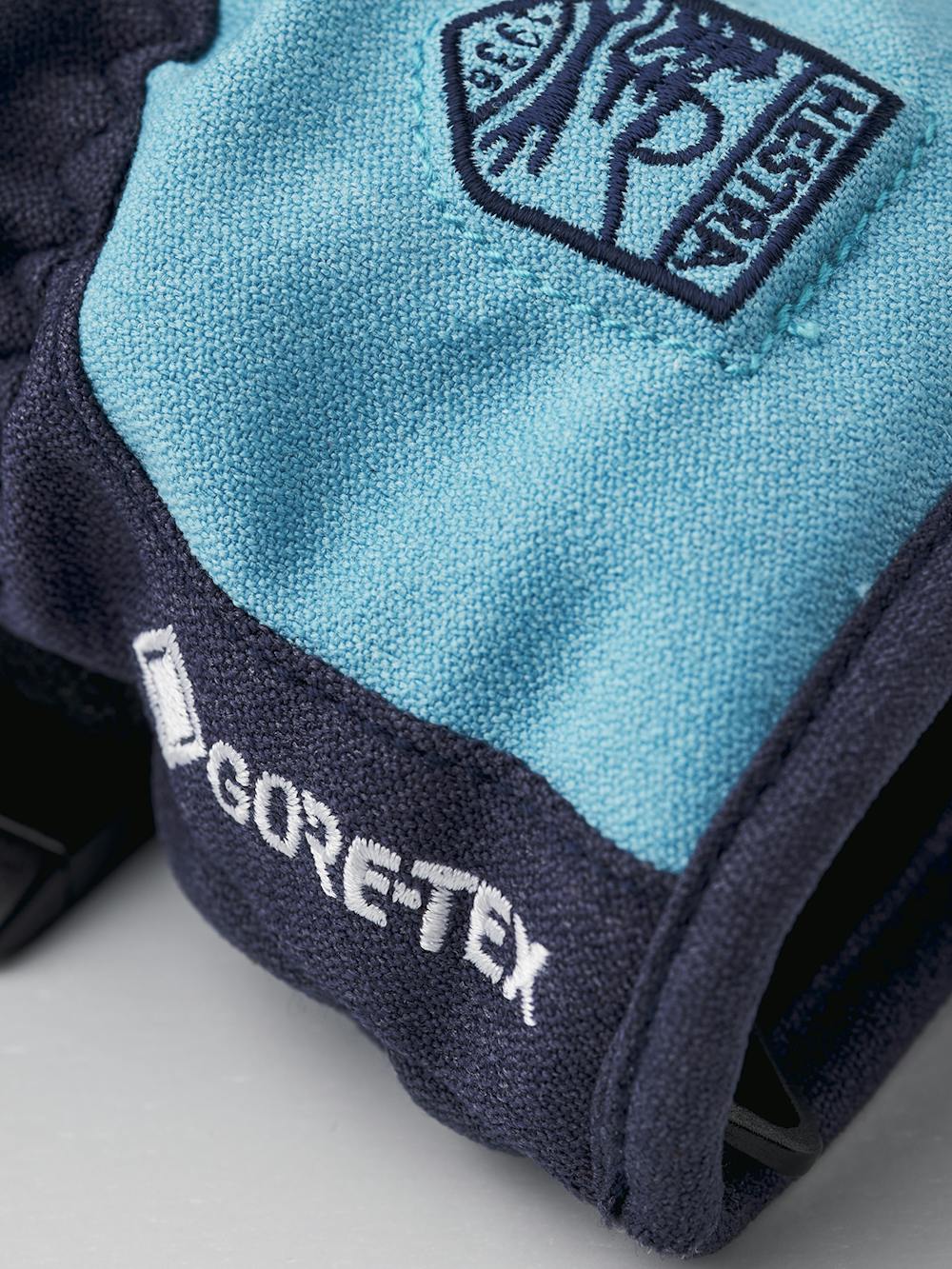 Blå barnhandske i tyg med svart syntetmaterial i innerhanden och handledsjustering 
 (4 av 6)